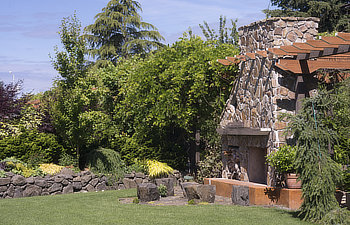 Untitleda massive fireplace with sitting Stones in front of it in a beautifully landscaped garden with a dry stone wall in the background at the edge of tall arbor walkway