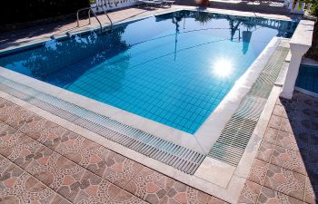 A clear blue swimming pool with a tiled deck reflecting sunlight and surrounded by a white railing.